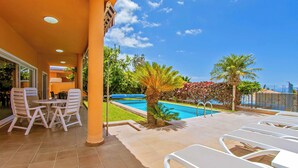 Zona junto a la piscina con sillones, una mesita y vistas al agua y la vegetación circundante.
