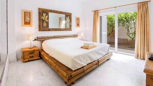 Un dormitorio con una cama grande, cabecera de madera, una mesita de noche con lámpara, un espejo y vistas al exterior a través de un ventanal corredero.