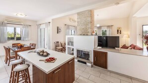 Una cocina moderna con una isla central, comedor con sillas, chimenea y televisor.