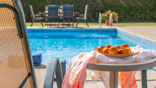 Un área junto a la piscina con una mesa que sostiene naranjas y una silla con una toalla.
