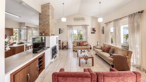 Un salón amplio con cocina, un ventanal con cortinas y una chimenea de piedra.