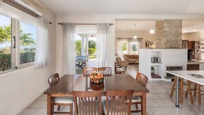 Un amplio comedor con una mesa y sillas de madera, un frutero y vistas al exterior a través de grandes ventanales.