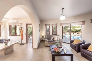 A spacious living area with a sofa, coffee table, and a view of an outdoor pool. - Stavros Villa - Four Bedroom Villa, Sleeps 8 (Poli Crysochous)