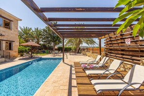 Een zwembadgedeelte met een houten pergola, ligbedden en uitzicht op zee.