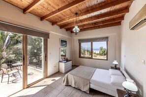 Een slaapkamer met een houten plafond, een bed, nachtkastje, dressoir en een balkon met tuinmeubilair.