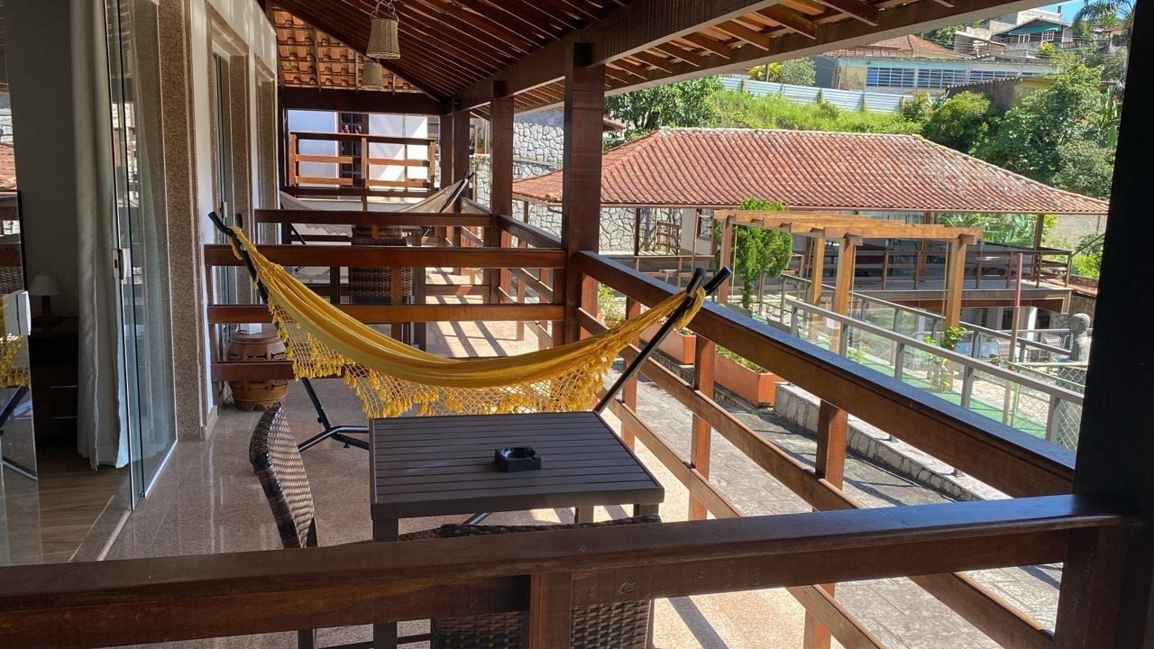 A balcony with a hammock, wooden furniture, and a view of buildings and greenery.