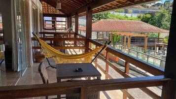 A balcony with a hammock, wooden furniture, and a view of buildings and greenery.