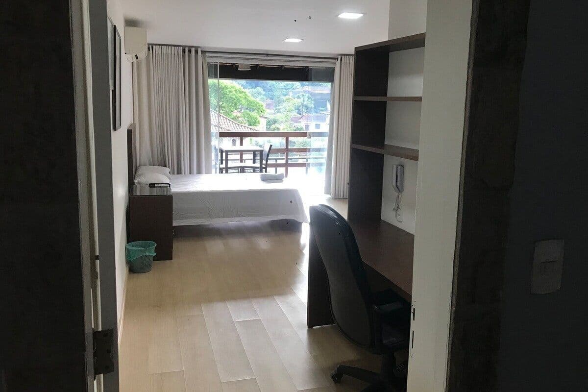 Una habitación con cama, escritorio, silla, ventana con cortinas y vista a zonas verdes.