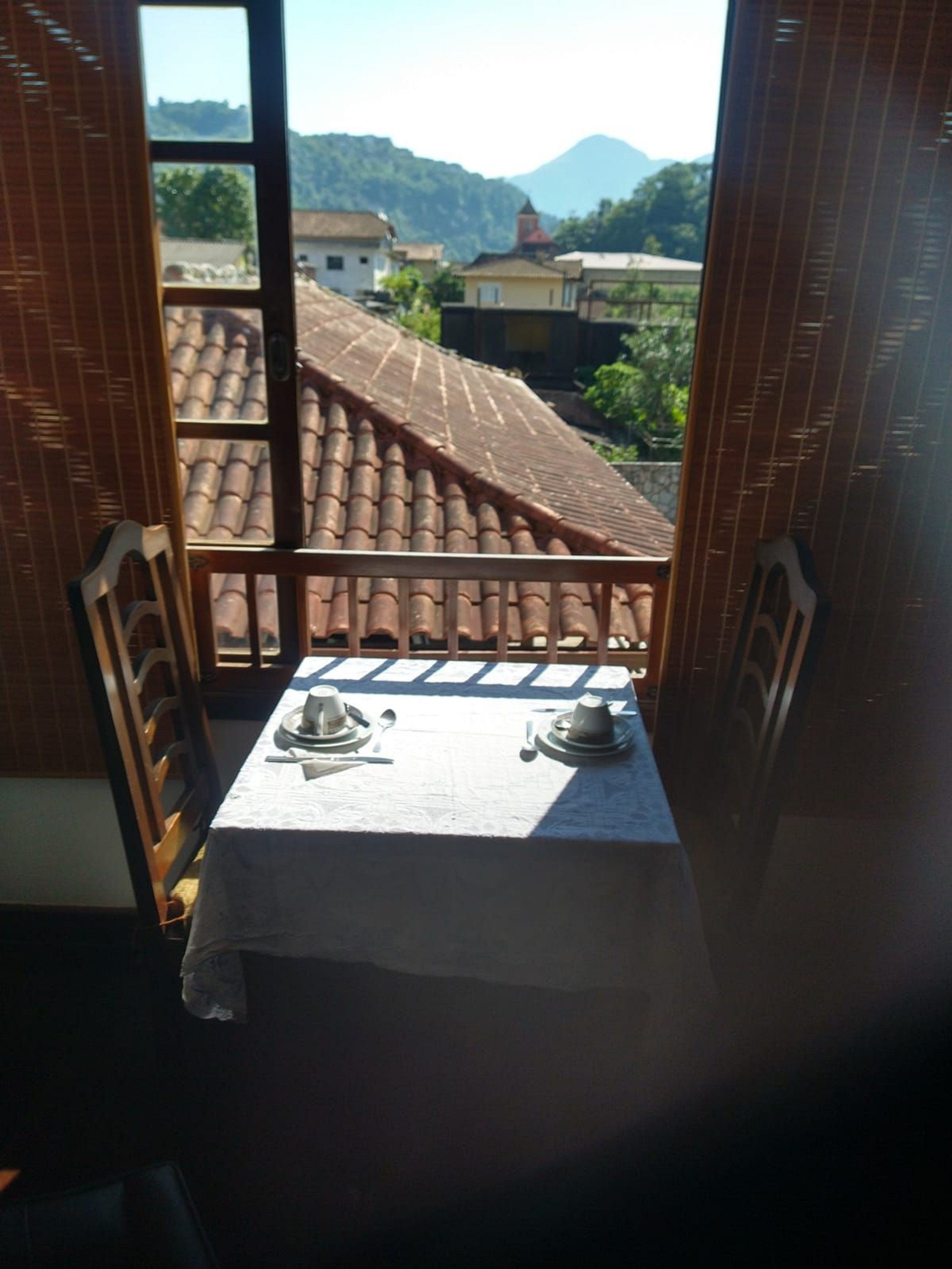 A balcony with a table set for two, overlooking a mountainous landscape.