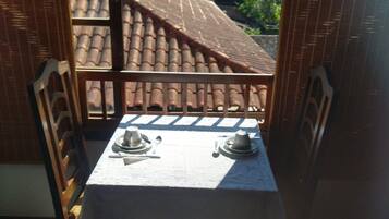 A balcony with a table set for two, overlooking a mountainous landscape.
