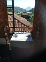 A balcony with a table set for two, overlooking a mountainous landscape.