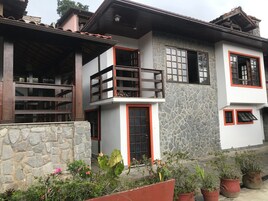 Una casa de dos plantas con fachada de piedra, un balcón con barandilla de madera y una puerta con marco rojo.
