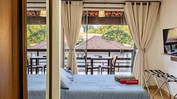 Une chambre à coucher avec un lit, une télévision et une vue sur une terrasse extérieure équipée d’une table et de chaises.