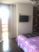 Un dormitorio con una cama, un televisor montado en la pared y una estantería.