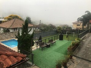 Zona de piscina en la azotea con césped artificial verde, una pared de piedra y vistas despejadas del vecindario circundante.