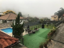 Zona de piscina en la azotea con césped artificial verde, una pared de piedra y vistas despejadas del vecindario circundante.