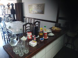Un comedor con una mesa preparada para cuatro, sillas, una cafetera y diversos alimentos.