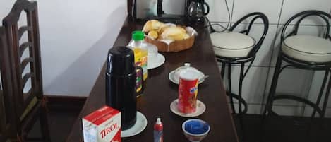 A dining table with various items including a box of TIROL, a coffee maker, a basket of bread, and several cups and bowls.