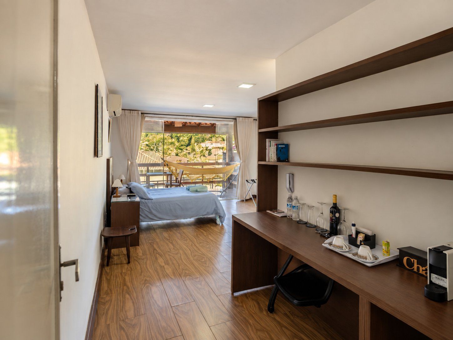 A hotel room with a bed, desk, chair, and a view of the outdoors.