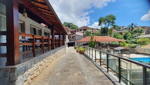Balcó empedrat de pedra amb barana de vidre que faiguellet a una piscina i una zona residencial.