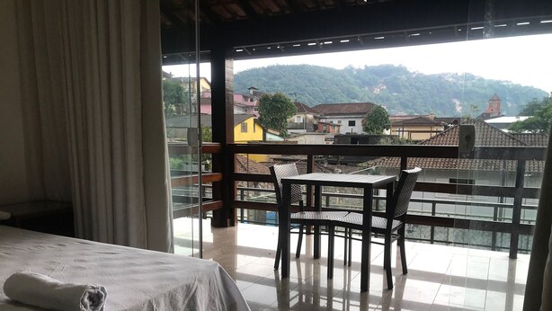 Habitació d'hotel amb un llit, una taula i cadires a un balcó que ofereix vistes a una vila i a les muntanyes.