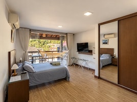 Un dormitorio con cama, mesita de noche, televisor y balcón con hamaca.