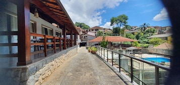 Un balcón con pavimento de piedra y baranda de cristal con vistas a una piscina y una zona residencial.