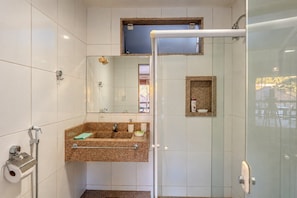 A bathroom with a shower, a sink with a mirror, and a small shelf with toiletries.