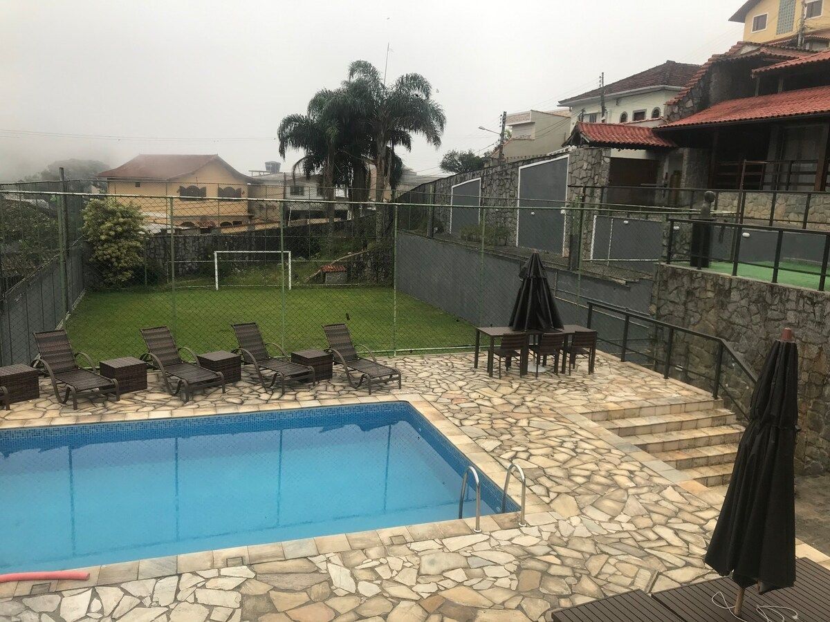 A swimming pool with lounge chairs and a table, surrounded by stone tiles and a stone wall.