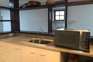 Una cocina con un lavamanos de acero inoxidable, un microondas y una ventana con vistas al exterior.