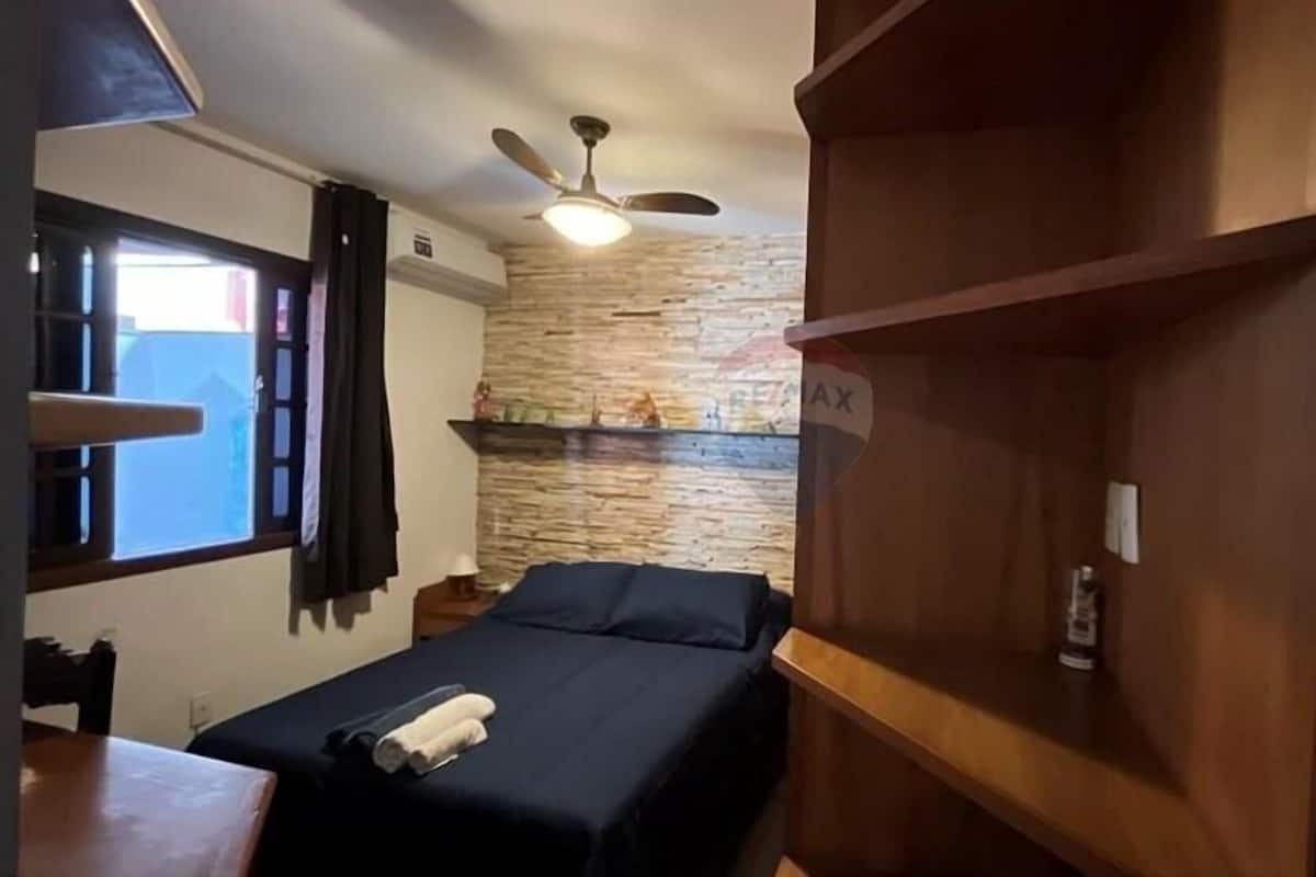 Un dormitorio con cama, ventilador de techo, pared de piedra y repisa de madera.