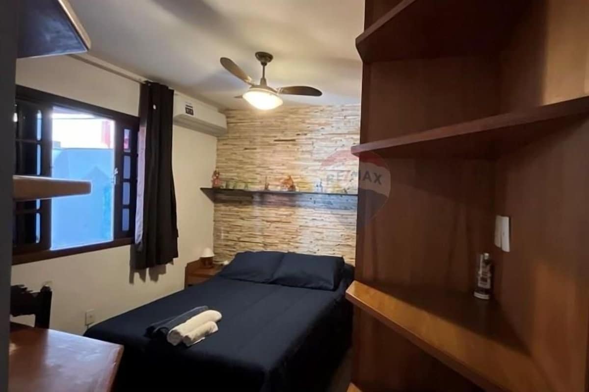 A bedroom with a bed, a ceiling fan, a stone wall, and a wooden shelf.