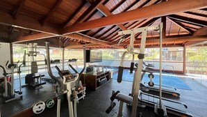 Un gimnàs amb diverses màquines d'exercici, incloent esteves i aparells de musculació, sota un sostre de fusta amb grans finestres.