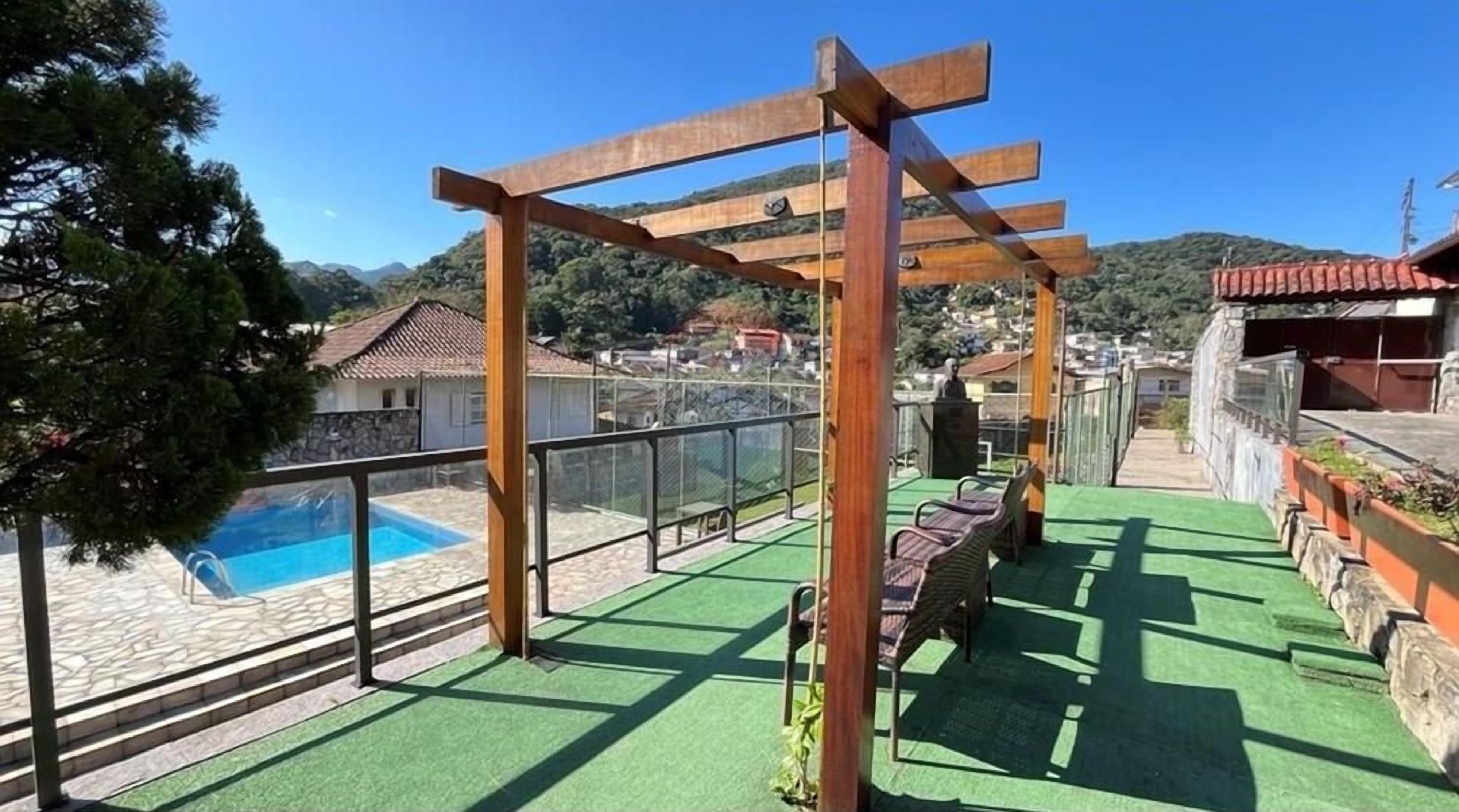 A rooftop terrace with a pool, green flooring, and wooden pergola.