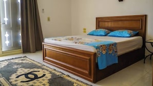 A bedroom with a wooden bed, blue and floral bedding, a patterned rug, and a window with curtains. - WHITE VILLA No. 8
 (Hurghada)