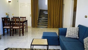 A living room with a blue sofa, a small table, and a dining area with chairs. A staircase is visible in the background. - WHITE VILLA No. 8
 (Hurghada)