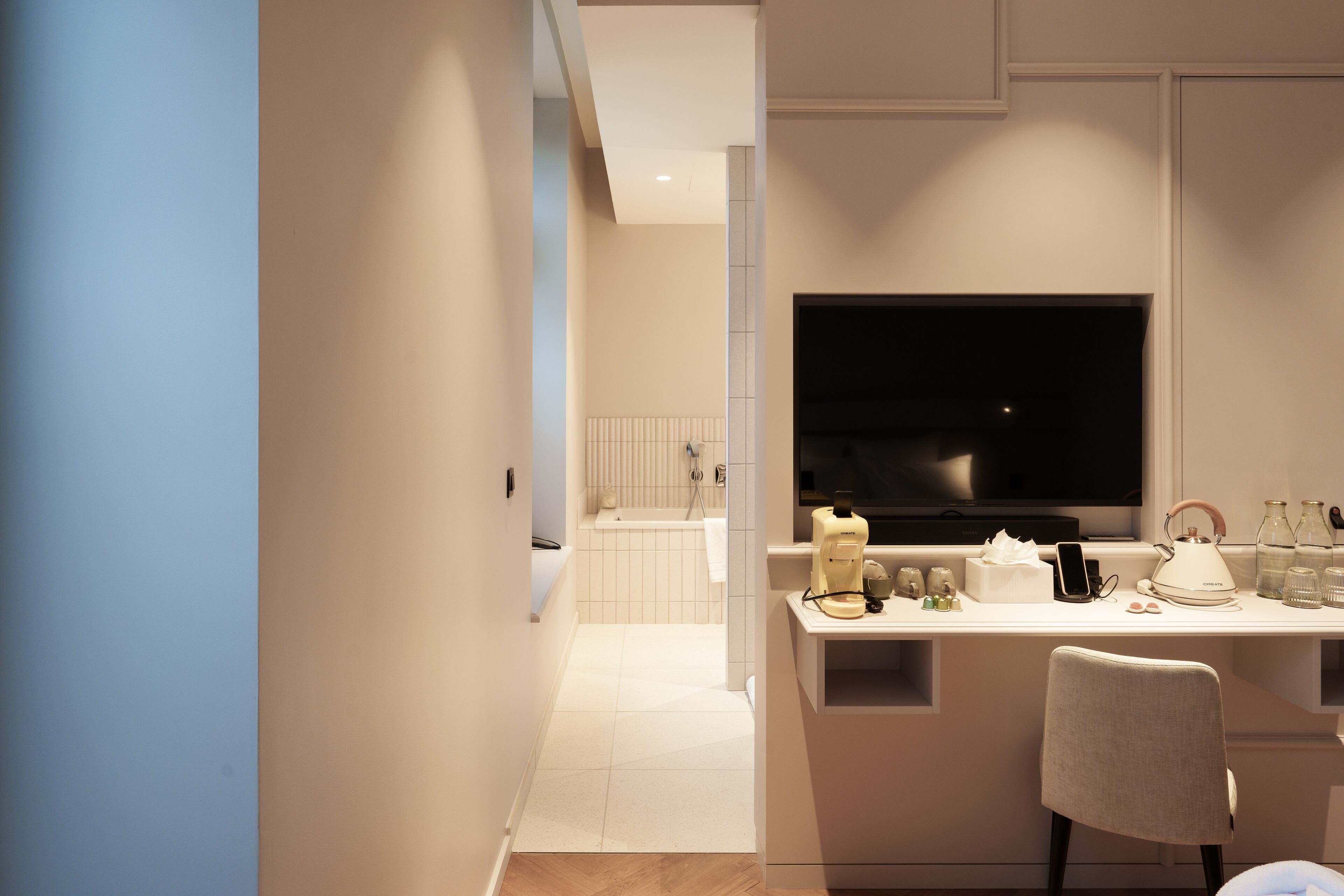 A modern bathroom with a bathtub, toilet, and sink. There is a vanity with a mirror and a television mounted above it.