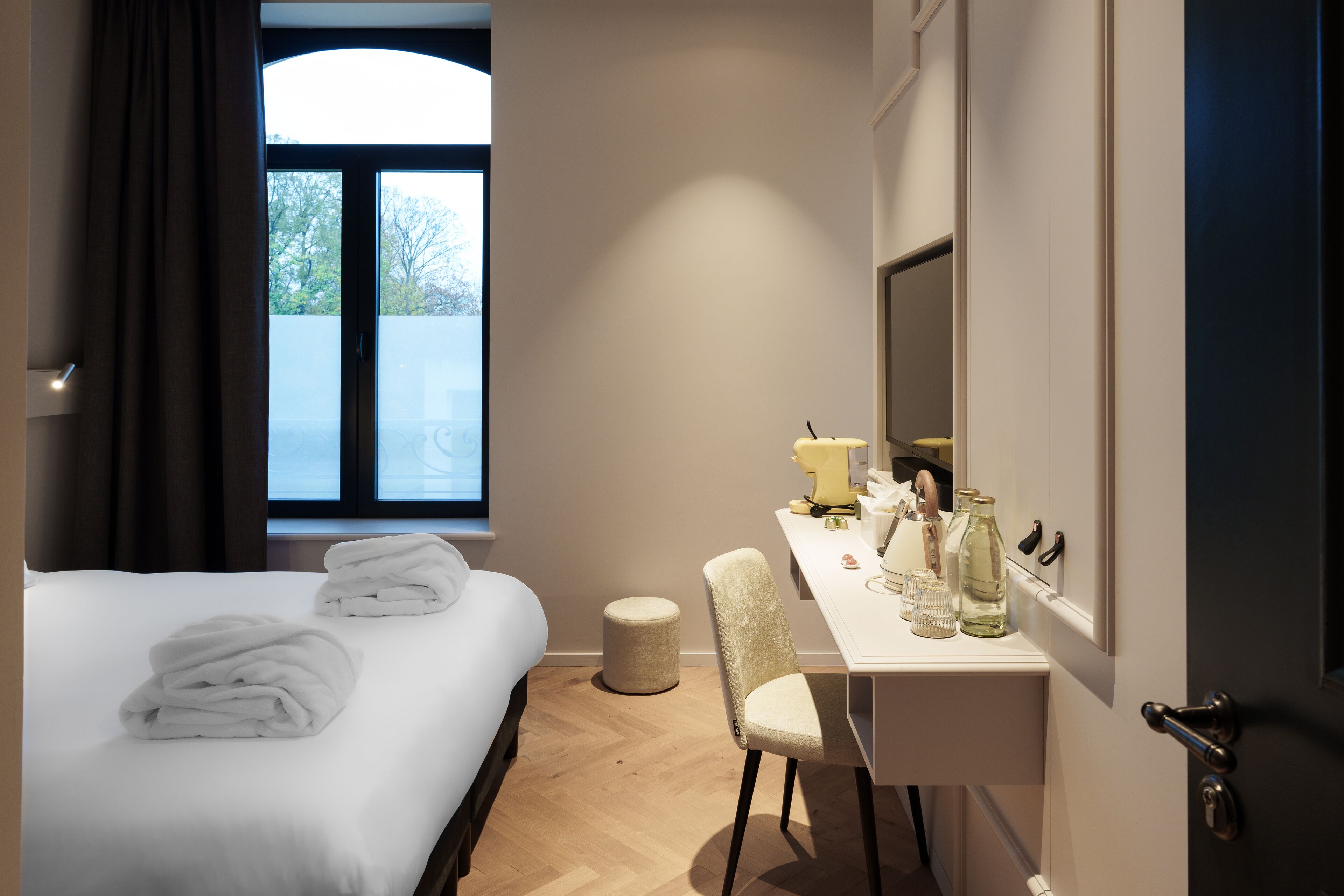 A hotel room with a bed, a desk, a chair, a window, and a mirror.