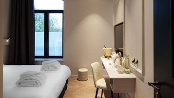 A hotel room with a bed, a desk, a chair, a window, and a mirror.