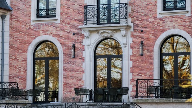 Un edificio con fachada de ladrillo, ventanas de arco y un balcón con barandilla de metal.