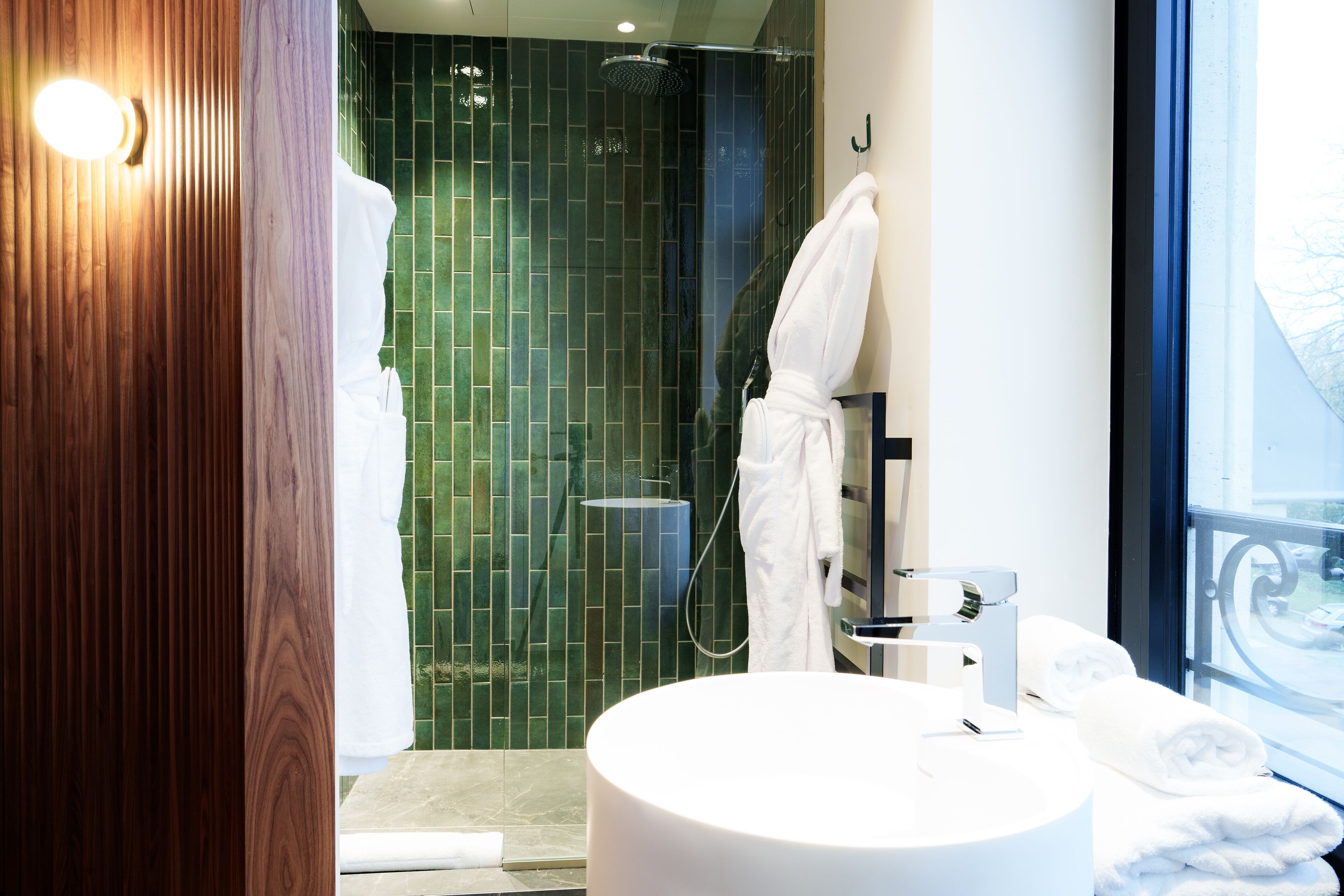 A modern bathroom with a round sink, a glass shower enclosure, and a view of the outdoors through a large window.