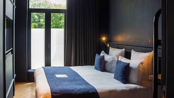 A modern hotel room with a large bed, a nightstand, and a view of the outdoors.