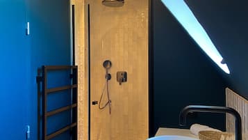 A modern bathroom with a large white sink, a glass-enclosed shower, and a dark blue accent wall.