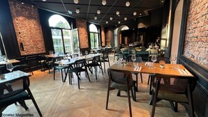 Un restaurante con paredes de ladrillo, ventanas amplias y varias mesas dispuestas con sillas y copas de vino.