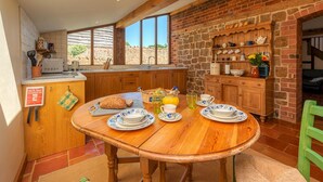 Una cocina acogedora con armarios de madera, una mesa de comedor dispuesta con platos, y una pared de ladrillo.