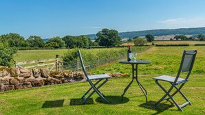 Un espacio al aire libre con césped, con dos sillas de metal y una mesa, una botella de vino y una copa.