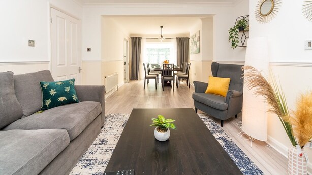 Uma sala de estar moderna com um sofá, poltrona e mesa de centro, que se abre para uma área de jantar com mesa e cadeiras.