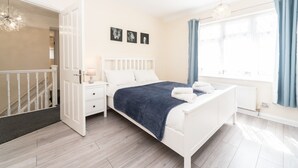 Quarto com cama, mesas de cabeceira, cômoda, lustre e janela com cortinas.