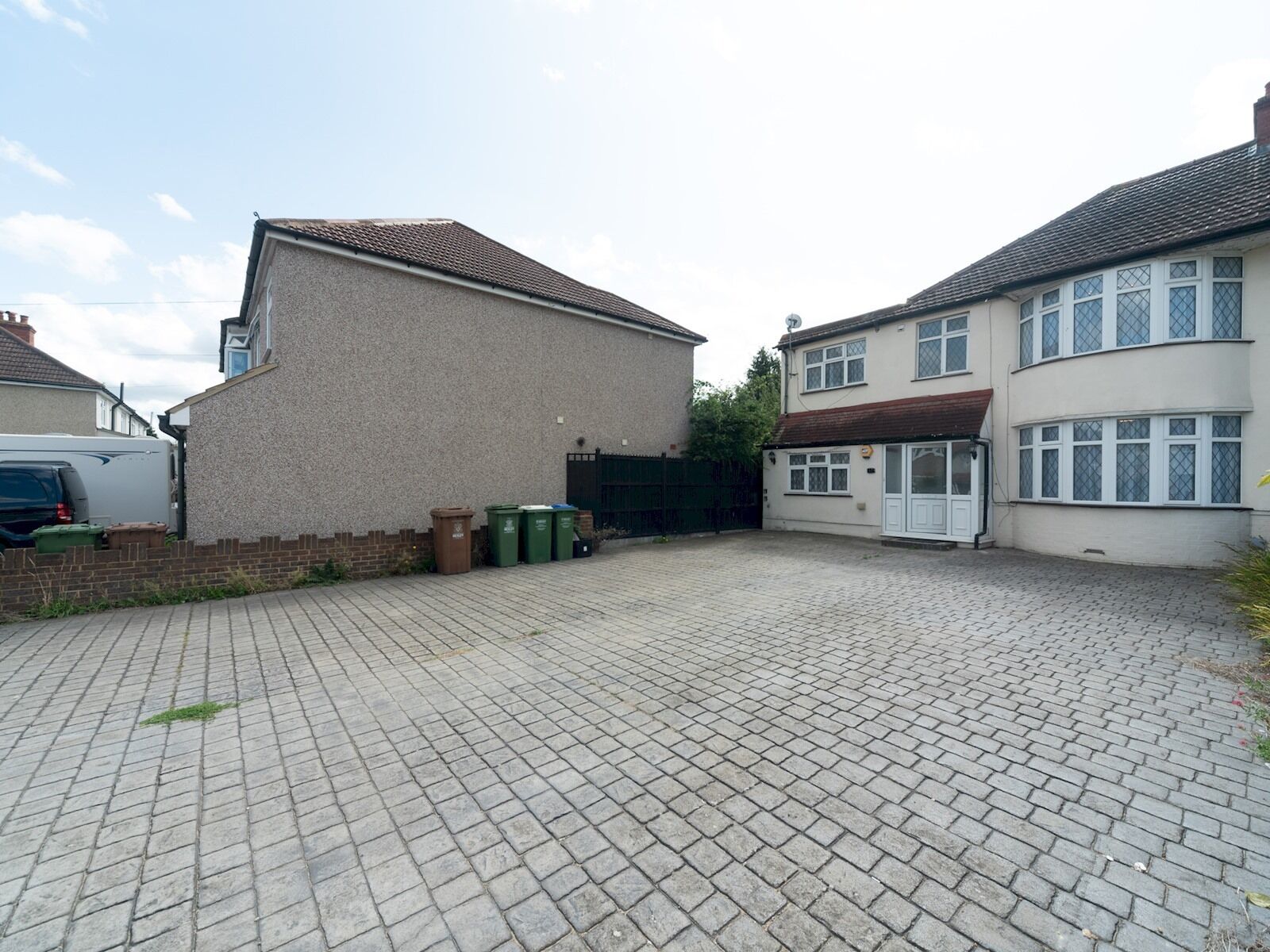 A paved courtyard with two houses, one with a white facade and the other with a beige facade, and a parked car.