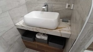 Casa de banho com uma pia branca, bancada de mármore e duas gavetas de arrumação.